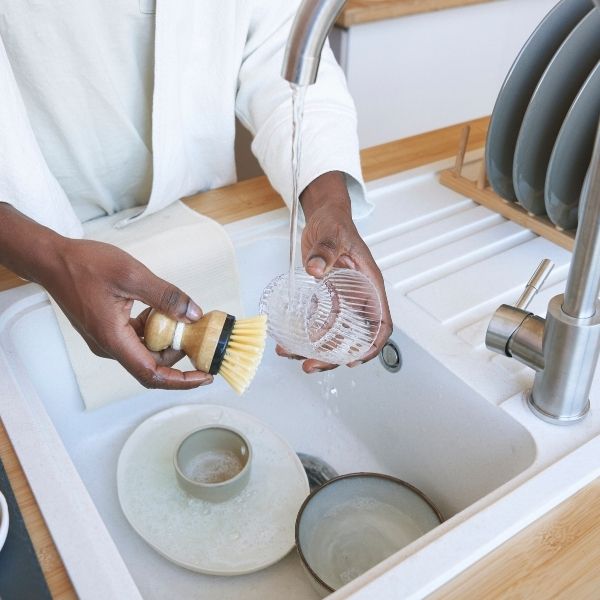 person washes dishes by hand in the kitchen sink with a brush
